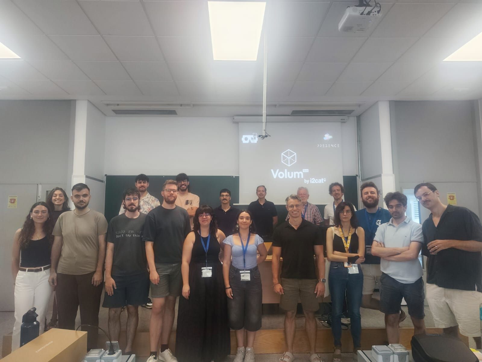 Group photo of colleagues and students in a presentation room, with the Volum by i2CAT and PRESENCE logos projected on the wall behind them
